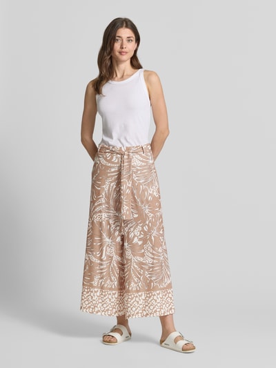 Modelka nosi Stoffhose mit Bindegürtel od More & More, beżowy materiałowy melanż ze stretchem, krój relaxed fit, wzór allover, pasek, szerokość w rozmiarze 36: 38 cm, długość nogawki od wewnątrz w rozmiarze 36: 64 cm, widok całej sylwetki z przodu.