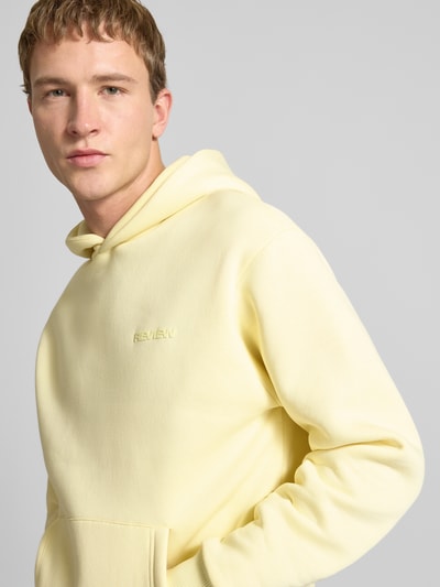 Männermodel trägt Regular Fit Hoodie mit Logo-Print von Review in lichtgeel, katoenmix, met capuchon en kangoeroezak, Nahaufnahme Oberkörper