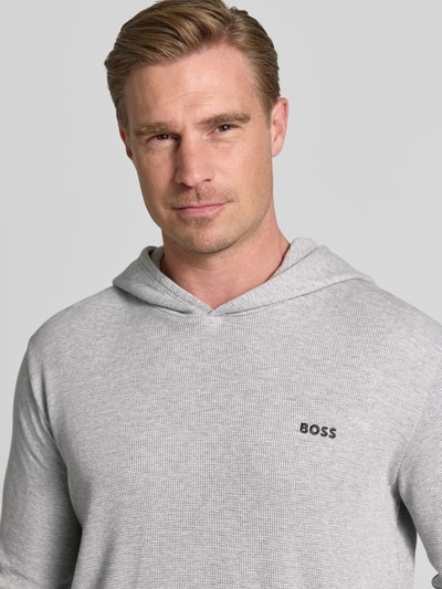 Mężczyzna nosi Regular Fit Hoodie aus Baumwoll-Mix von BOSS w jasnoszarym kolorze, drobna struktura materiału, Nahaufnahme górnej części ciała.