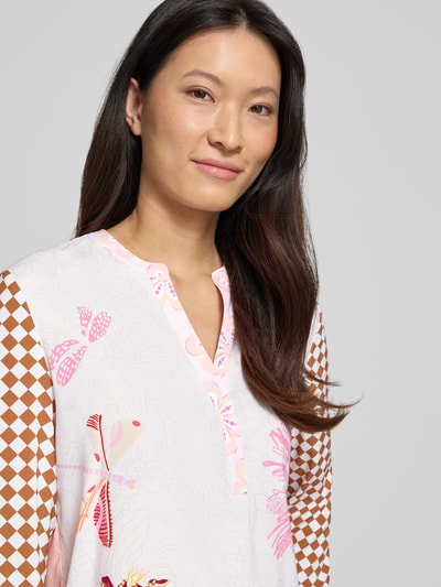 Vrouwenmodel draagt Relaxed Fit Tunika-Bluse aus Seiden-Mix van HERZENS met bloemen all-over print, elastische zijdemix, tuniekhals, langärmelig, ruglengte maat 36: 70 cm, mouwlengte maat 36: 64 cm, detailopname bovenlichaam.