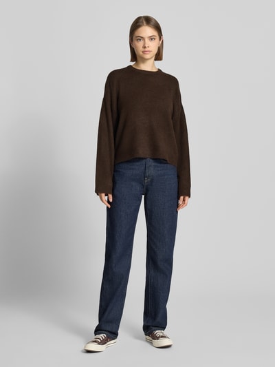 Frauenmodel trägt Relaxed Fit Pullover mit Rundhalsausschnitt Modell 'SIMONI' von ONLY in Dunkelbraun zu blauer Jeans, Ganzkörperansicht von vorne, Damen Pullover von ONLY.