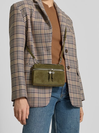 Vrouwenmodel draagt Crossbody Bag met Label-Print van Tory Burch in olijfgroen suède, tweezijdige ritssluiting, afneembare schouderriem, kort handvat, binnenvak, hoofdvak, 18x12x6 cm, voorkant bovenlichaam close-up.