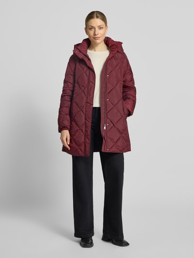 Vrouwenmodel draagt Regular Fit lange jas in stiksels van FUCHS SCHMITT, bordeaux, steekzakken, capuchon met opstaande kraag, helemaal van voren