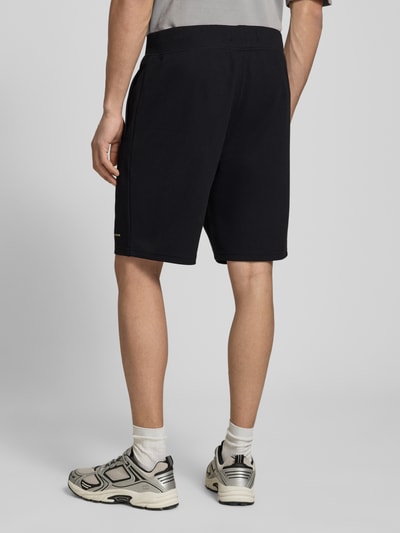 Männermodel trägt Straight Fit Shorts mit Strukturmuster von G-Star Raw in Schwarz mit Logo-Detail, Elastischer-Material-Mix, Rückansicht Ganzkörperansicht.