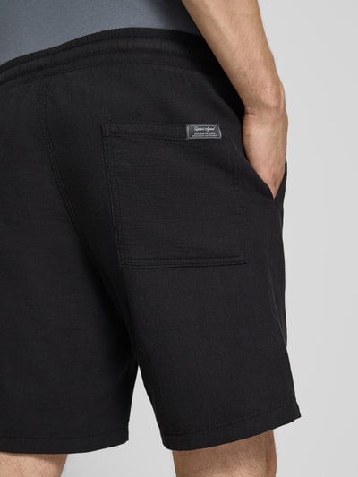 Männermodel trägt Shorts met structuurpatroon model 'JAIDEN' van Jack & Jones, zwarte katoenen regular fit, elastische taille met tunnelkoord, productdetail, detailopname achterzijde.
