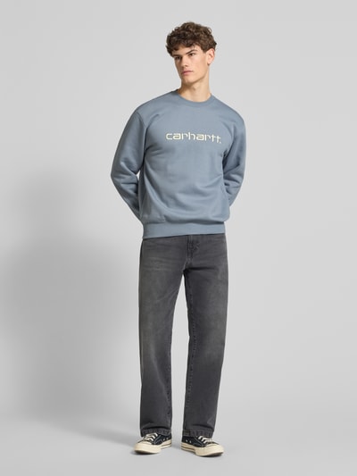 Männermodel trägt Sweatshirt mit Label-Stitching von Carhartt Work In Progress in Blau, lockere Passform, Ganzkörperansicht von vorne.