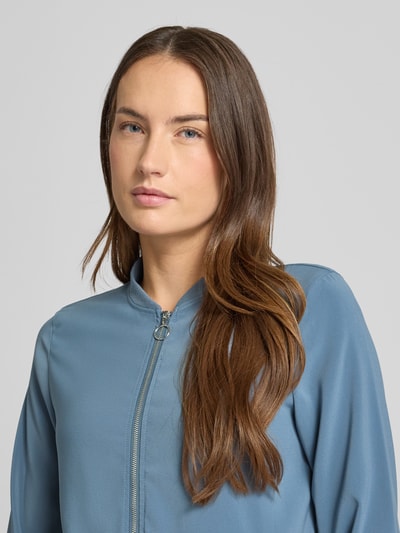 Modelka kobieca nosi Regular Fit Bomberjacke mit College-Kragen Modell 'COCO' od Vero Moda, kolor jednolity, faktura gładka, zamek błyskawiczny, długie rękawy z ściągaczami, boczne kieszenie; zbliżenie na górną część ciała.