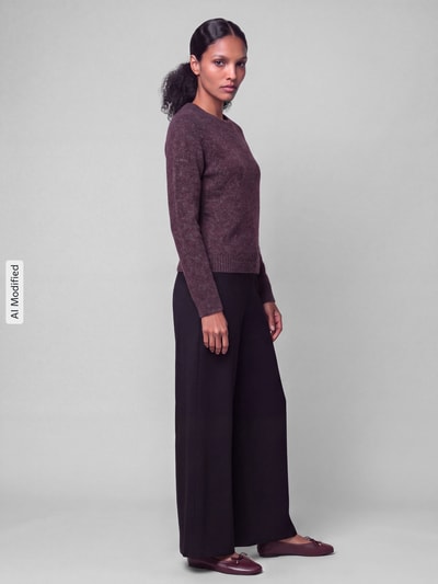Frauenmodel trägt Regular Fit Pullover mit Rundhalsausschnitt Modell 'DOFFY' von VERO MODA in Dunkelbraun, kombiniert mit schwarzer Hose, Ganzkörperansicht von vorne, KI-modifiziertes Bild.