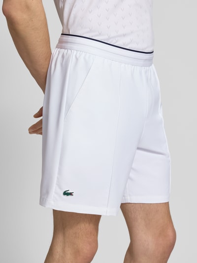 Männermodel trägt Regular Fit Sport-Shorts mit elastischem Bund von Lacoste Sport, unifarben weiß, Logo-Patch, seitliche Taschen, Nahaufnahme Oberschenkel.