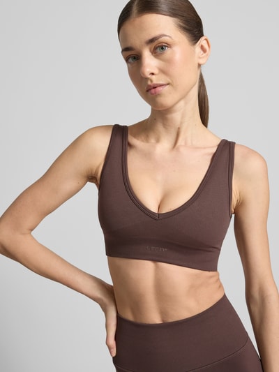 Frauenmodel trägt Regular Fit Bustier mit Logo-Detail von aim'n, brauner Farbton, elastisches Material, Logo und Bund sichtbar, Nahaufnahme Oberkörper.