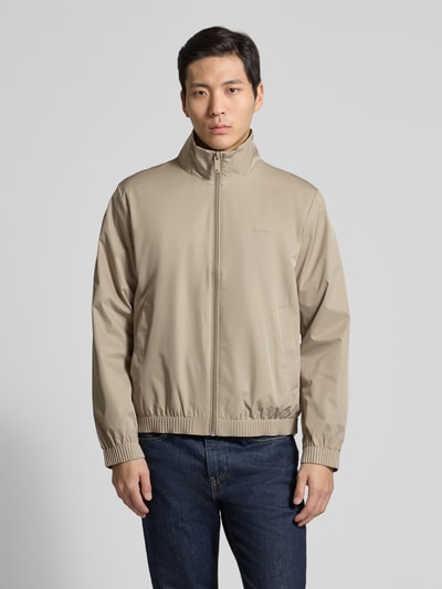Männermodel trägt Jacke mit Stehkragen und Reißverschluss von CK Calvin Klein in Beige, glatte Textur, Regular Fit, Eingrifftaschen, Ganzkörperansicht von vorne. Rückenlänge 65 cm, Schulterbreite 46 cm, Brustweite 57 cm, Ärmellänge 67 cm.