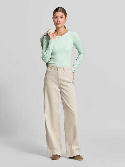 Modelka nosi bluzkę z długim rękawem Longsleeve aus Baumwoll-Mix von Marc Cain w kolorze miętowym, krój slim fit, okrągły dekolt, mieszanka bawełny i elastanu, długość tyłu w rozmiarze 36: 50 cm, jasnobeżowe szerokie spodnie, brązowe buty, gładkie tło, całkowity widok z przodu.