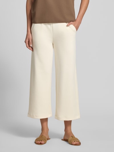 Kobiece model prezentuje spodnie dresowe Wide Fit Sweatpants in verkürzter Passform Modell 'Banu' od Soyaconcept, elastyczna mieszanka materiałów z domieszką modalu, kolor jasny kremowy, szerokie nogawki, skrócony krój, elastyczny pas z tunel, widok na nogi z przodu, zbliżenie dolnej części ciała.