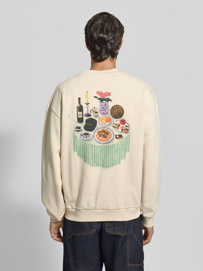 Mężczyzna nosi Sweatshirt mit Label-Print und Rundhalsausschnitt od Les Deux z bawełny w kremowym kolorze, widok całej sylwetki od tyłu. Relaxed Fit, nadruk na plecach, długość tyłu 67 cm, długość rękawa 64 cm, model Cole Table.
