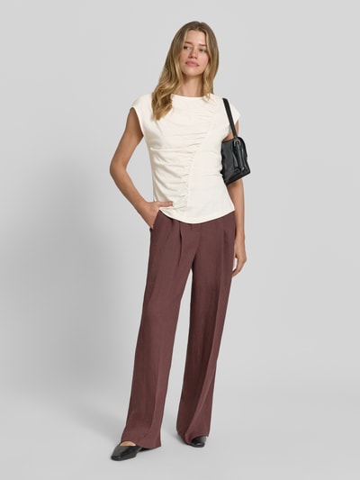 Vrouwenmodel draagt T-shirt met ronde hals en draperingen van Christian Berg Woman, mix van katoen en micromodal, slim fit, kapmouwen, ruglengte maat S 56 cm, crèmekleurig met zachte textuur, gecombineerd met wijde bordeauxrode broek. Volledige lichaamsweergave van voren.