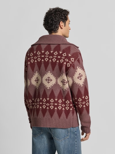 Männermodel trägt Strickjacke mit abstraktem Muster von DRYKORN in Rot- und Beigetönen, reine Baumwolle, Rückansicht, Ganzkörperansicht.