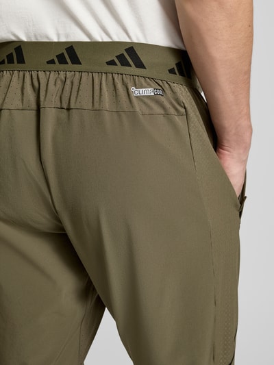 Männermodel trägt Regular Fit Sweatpants mit elastischem Bund mit Logo-Print Modell 'TECH APP S-PANT' von adidas Training in Optik: Unifarben, Materialverarbeitung: Batist, mit seitlichen Eingrifftaschen und Kontrastnähten, Nahaufnahme Rückansicht.