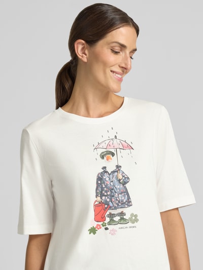 Vrouwenmodel draagt Regular Fit T-shirt uit puur katoen van Marc Cain met logoprint en motiefprint, ronde hals, ruglengte maat 36: 58 cm, close-up bovenlichaam.