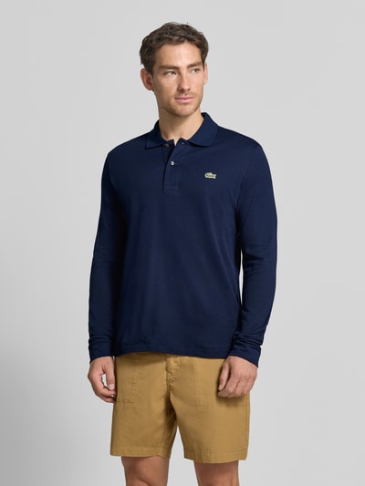 Männermodel trägt Regular Fit Poloshirt aus reiner Baumwolle von Lacoste in Dunkelblau zu beigefarbenen Shorts, Ganzkörperansicht von vorne, Herren Poloshirt von Lacoste.
