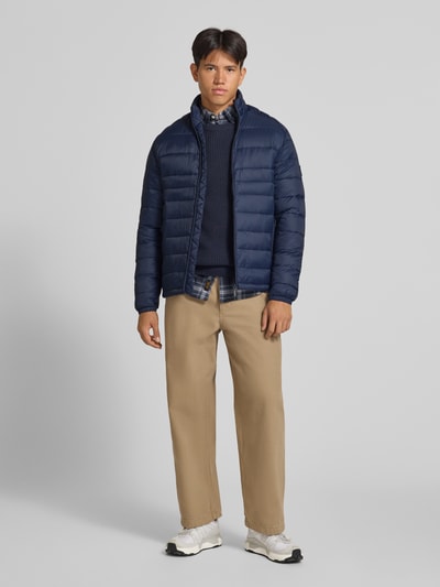 Mężczyzna model nosi Regular Fit kurtkę z efektem pikowania Model 'Kingsley' od JACK & JONES, granatowa, stójka, zamek błyskawiczny, wpuszczane kieszenie, długość tyłu w rozmiarze M: 72 cm, szerokość ramion w rozmiarze M: 48 cm, szerokość w rozmiarze M: 51 cm, długość rękawów w rozmiarze M: 68 cm, widok całej sylwetki z przodu.