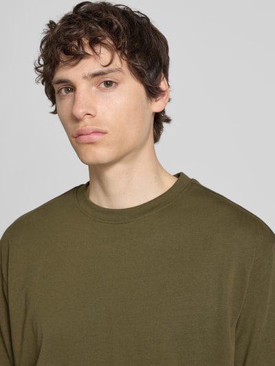 Mężczyznamodel nosi Oversized T-Shirt Modell 'FISHER' od Blend, bawełna, kolor oliwkowy, tkanina gładka, okrągły dekolt, koszulka o długości 72 cm w rozmiarze M, widok na górną część tułowia z przodu