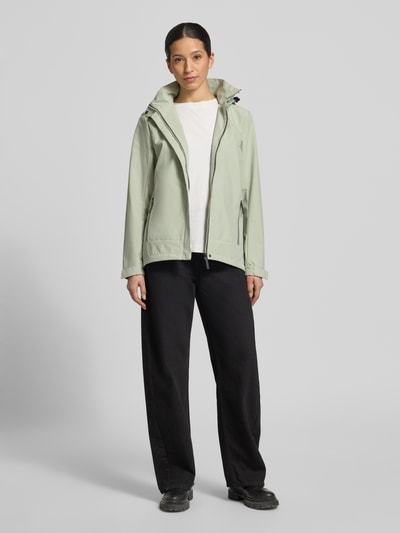 Frauenmodel trägt Parka mit Kapuze und verdecktem Reißverschluss von G.I.G.A. DX in hellem Grün, schwarze Hose, gerader Schnitt, Ganzkörperansicht von vorne, Produktdetails: Wassersäule 10.000mm, Kordelstopper an der Kapuze, seitliche Reißverschlusstaschen, Label-Patch, Maße bei Größe 36.