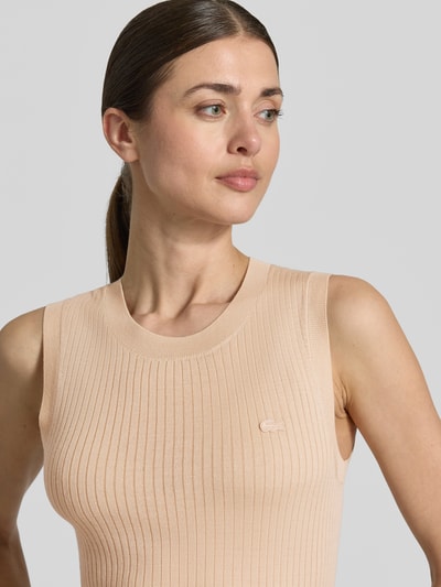 Frauenmodel trägt Slim Fit Pullunder aus reiner Wolle von Lacoste in Strickoptik mit Streifen-Struktur und Logo-Detail, Rippstrick, Farbe Beige, Nahaufnahme Oberkörper.