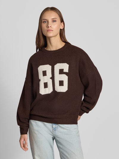 Vrouwenmodel draagt Regular Fit Pullover in tricotlook van REVIEW, materiaalmix met stretch, bruine kleur, geribde bies en ribboorden, lange mouw, oversized schouders, ruglengte maat S 59 cm, mouwlengte maat S 52 cm, voorkant van het bovenlichaam, KI-modified image.