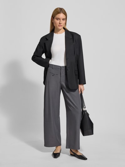 Kobiece modelka nosi spodnie materiałowe z wpuszczanymi kieszeniami model 'Massie' od Neo Noir, mieszanka materiałów z dodatkiem streczu, luźny krój, zapięcie na guzik i zamek błyskawiczny, szerokość w rozmiarze 36: 38 cm, długość wewnętrzna nogawki w rozmiarze 36: 76 cm, widok całej sylwetki z przodu.