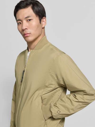 Männermodel trägt Blouson mit Label-Detail Modell 'MILD' von GOFRANCK in Beige, glatte Oberfläche, Reißverschluss, Nahaufnahme Oberkörper.
