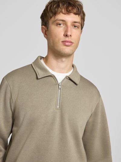 Männermodel trägt Regular Fit Sweatshirt mit Baumwoll-Anteil Modell 'Bradley' von JACK & JONES in Beige, Nahaufnahme Oberkörper, Troyer-Kragen und Reißverschluss, angenehmer Material-Mix, Rückenlänge 69 cm bei Größe M.