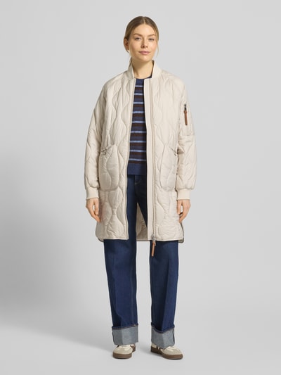 Frauenmodel trägt Steppmantel mit Ärmeltasche Modell 'AVON' von Beaumont Amsterdam in Beige, gerade Passform, Ganzkörperansicht von vorne.