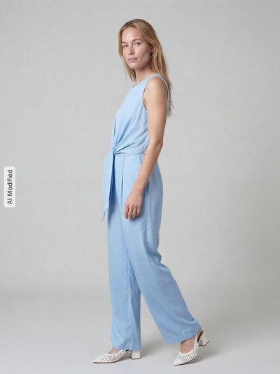 Frauenmodel trägt Jumpsuit aus Satin mit Bindegürtel von Christian Berg Cocktail in Hellblau, glatte Textur, Ganzkörperansicht von vorne. Leicht taillierte Passform, Rundhalsausschnitt, Bindegürtel auf Taillenhöhe, Nahtreißverschluss hinten, gerades Bein.