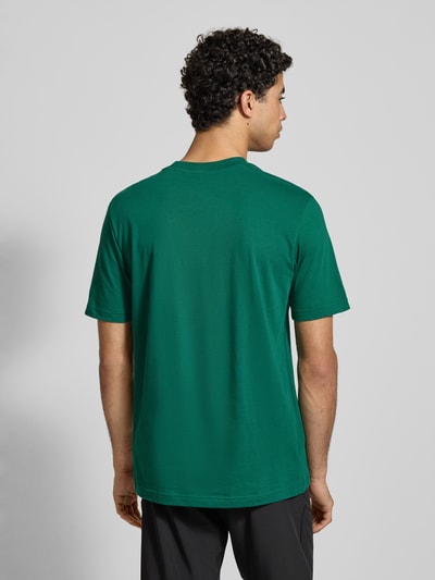 Männermodel trägt T-Shirt mit Label-Print von adidas Sportswear in Grün, Reine Baumwolle, Regular-Fit, Rückenlänge 75 cm, Ganzkörperansicht Rückansicht.