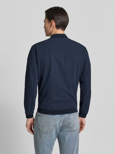 Männermodel trägt dunkelblaue Regular Fit Jacke mit Stehkragen Modell 'Campo' von SCANDINAVIAN EDITION, Ganzkörperansicht Rückansicht, glatte Textur, sichtbare Abschlüsse:, kombiniert mit blauer Jeans, laut Kontext Zweiwege-Reißverschluss, Eingrifftaschen, elastische Abschlüsse:, Rückenlänge bei Größe M 67 cm, Schulterbreite 44 cm, Brustweite 51 cm, Ärmellänge 64 cm.
