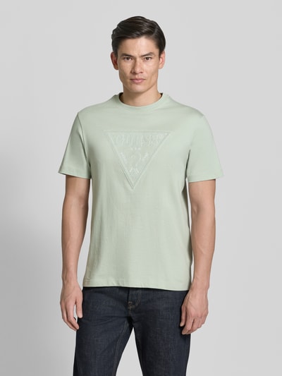 Männermodel trägt T-Shirt mit Logo und Rundhalsausschnitt von Guess, Herren T-Shirt aus reiner Baumwolle, Regular-Fit, Ganzkörperansicht von vorne. Rückenlänge bei Größe M: 70 cm.