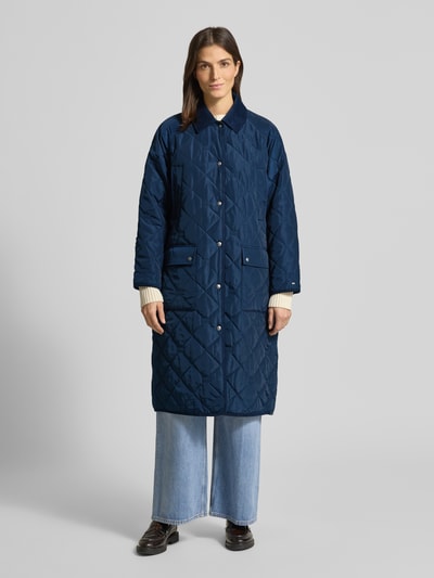 Vrouwenmodel draagt Regular Fit Steppmantel met Logo-Details van Tommy Hilfiger in effen donkerblauw met cordkraag en opgestikte zakken, Ganzkörperansicht von vorne.