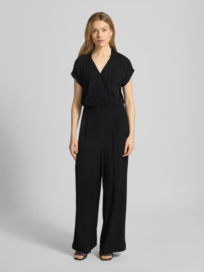 Modelka kobieca nosi Jumpsuit aus Viskose mit V-Ausschnitt Modell 'MARRAKECH' von ICHI, czarny, krój slim fit, tkanina lekko połyskująca, szerokie nogawki, dekolt V, kieszenie, szerokość w rozmiarze S: 43 cm, długość całkowita: 146 cm, długość nogawki: 74 cm, widok całej sylwetki od przodu.