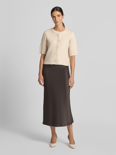 Frauenmodel trägt Regular Fit Cardigan in Strick-Optik Modell 'Iga' von VILA im elastischen Material-Mix, cremefarben mit 1/2-Arm und durchgehender Knopfleiste, kombiniert mit einem langen, braunen Rock, Ganzkörperansicht von vorne.
