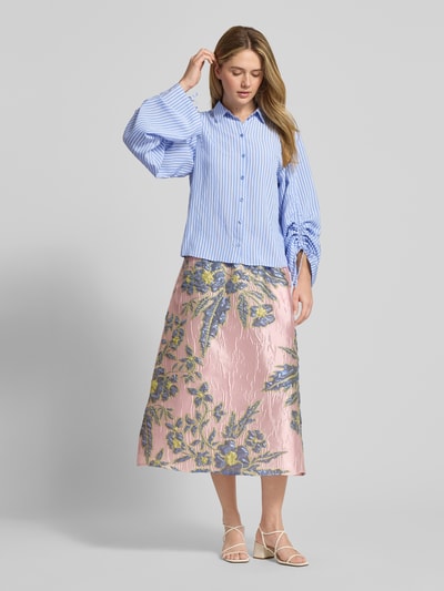 Frauenmodel trägt Relaxed Fit Bluse aus Viskose-Mix von Milano Italy mit Hemdblusenkragen und Ärmel mit Tunnelzug, gestreift in Blau, kombiniert mit gemusterter floraler Rocktextur, Ganzkörperansicht von vorne. Rückenlänge bei Größe 36: 57 cm, Ärmellänge: 68 cm.