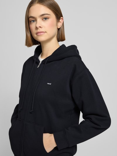 Kobiece model prezentuje Sweatjacke mit Reißverschluss od Levi's®, czarny bawełniany miks, luźny krój, kaptur, zbliżenie na górę.