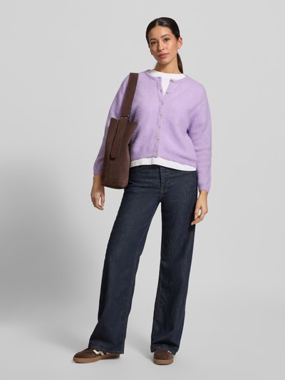 Vrouwenmodel draagt Strickjacke mit Knopfleiste Modell 'VITOW' van American Vintage, lila kleur, geribde boorden, ronde hals, ontspannen pasvorm, alpaca-wolmix met stretch, knoopsluiting, volledige lichaamsvooraanzicht.