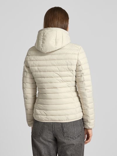 Frauenmodel trägt Steppjacke mit Kapuze Modell 'DAISY' von SAVE THE DUCK in Beige, körpernah, gesteppte Textur, Ganzkörperansicht Rückansicht. Passform, Maße und Kapuze laut Kontext.