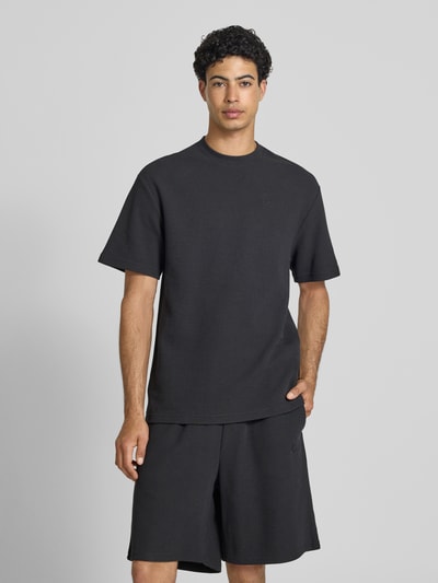 Männermodel trägt Oversized T-Shirt mit Strukturmuster und Logo-Stitching von KARL KANI aus Baumwoll-Mix, schwarze Farbe, Rundhalsausschnitt, Oversized-Fit, Herren T-Shirt, Rückenlänge 75 cm, Ganzkörperansicht von vorne.