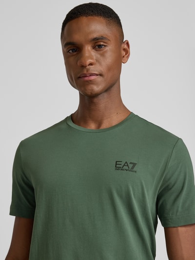 Männermodel draagt T-Shirt met Label-Print van EA7 Emporio Armani, groen, slim fit, rib kraag, katoen-elastaan, borstlogo, Nahaufnahme Oberkörper.