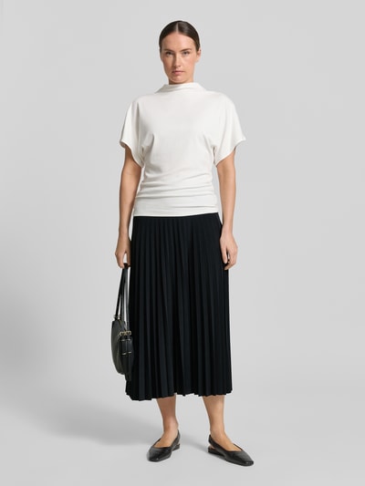 Frauenmodel trägt Midirock mit Plisseefalten von Rich & Royal im Material-Mix mit Stretch-Anteil, schlichter Look, Ganzkörperansicht von vorne.