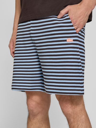 Männermodel trägt Regular Fit Sweatshorts aus Baumwoll-Mix von Lacoste mit blau-braunem Streifenmuster, Logo-Stitching, Nahaufnahme Oberschenkel.