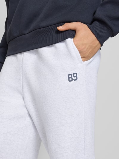 Männermodel trägt Straight Leg Sweatpants mit elastischem Bund von KARL KANI aus Baumwoll-Mix, Gesäßtasche, Nahaufnahme Oberschenkel.