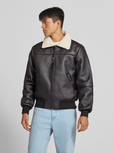Männermodel trägt schwarze Bomberjacke mit Kentkragen und gerippten Abschlüssen von Alpha Industries, beige Teddyfell, Vorderansicht, Nahaufnahme Oberkörper. Herren Bomberjacke mit Reißverschluss, Eingrifftaschen mit Druckknopfverschluss, Regular Fit, Maße: Rückenlänge 66 cm, Schulterbreite 48 cm, Brustweite 55 cm, Ärmellänge 70 cm.