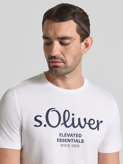 Mężczyzna nosi Regular Fit T-Shirt aus reiner Baumwolle Modell 'BASIC TEE BIG LOGO' von s.Oliver RED LABEL w kolorze białym z czarnym nadrukiem, widoczna faktura bawełny, Nahaufnahme Oberkörper.